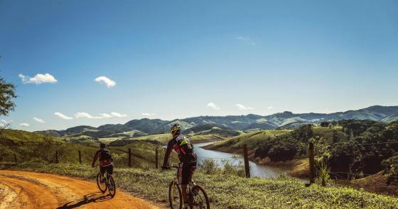 Ciclisti esplorano paesaggi collinari verdi sotto un cielo limpido e soleggiato.