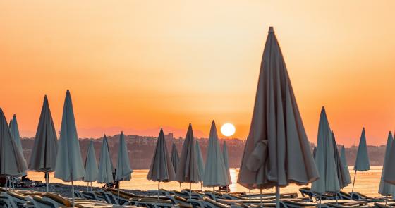 Tramonto arancione su spiaggia deserta con ombrelloni chiusi, atmosfera di pace e silenzio.