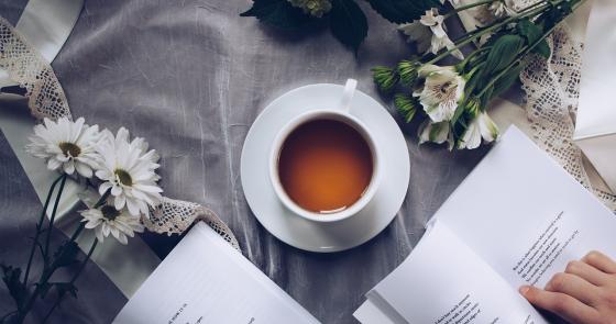 Tè caldo, poesie e fiori bianchi su una tovaglia elegante.