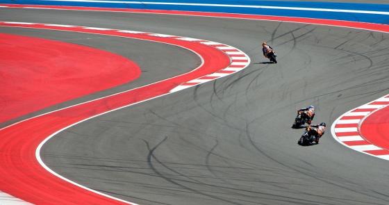 Tre moto sfrecciano su una pista colorata, curve emozionanti e velocità.