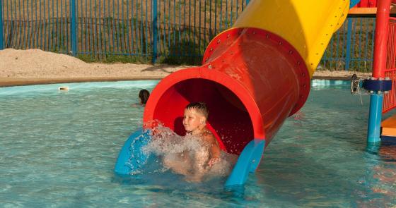 Bambino felice scivola in piscina, spruzzi d'acqua ovunque.