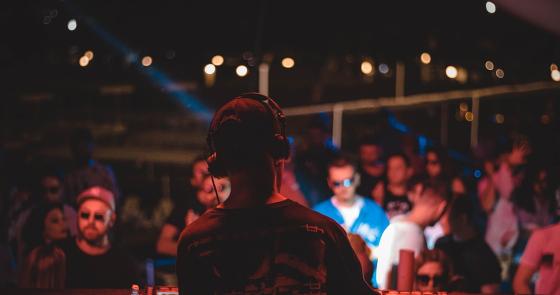 DJ suona in un club affollato, luci colorate e musica vibrante.