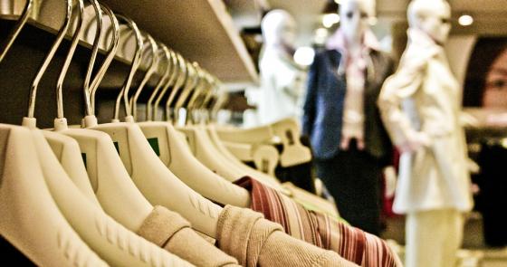 Abiti eleganti su appendini, manichini sfocati sullo sfondo, atmosfera di shopping raffinata.