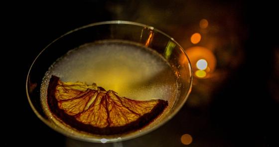 Cocktail elegante con fetta d'arancia essiccata, atmosfera calda e luminosa.