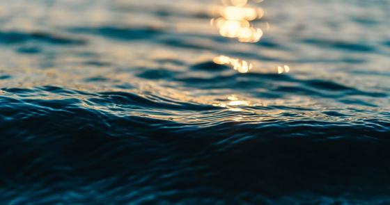 Onde blu scuro con riflessi dorati al tramonto, serenità e infinito.