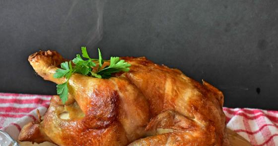 Pollo arrosto dorato e fumante, con prezzemolo fresco sopra, su tagliere di legno.