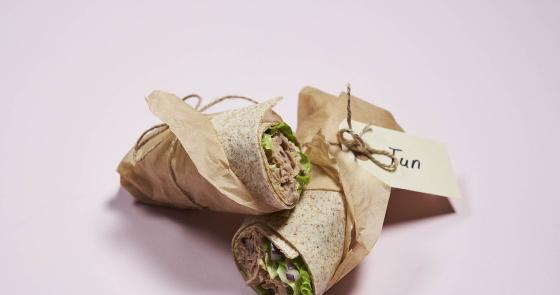 Due gustosi wrap di tonno avvolti in carta marrone su sfondo rosa.