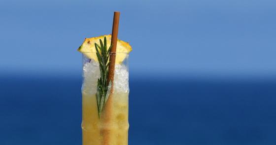 Cocktail tropicale rinfrescante con ananas e rosmarino, vista mare.