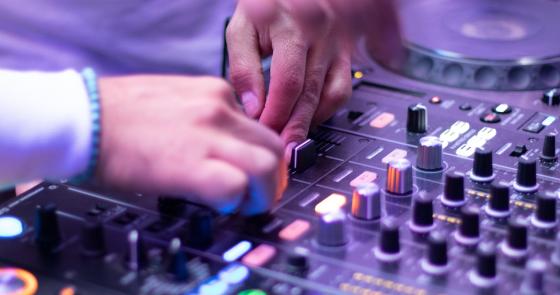Mani su console DJ, musica, luci, energia vibrante.