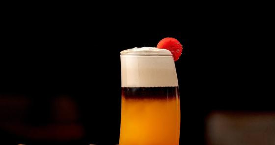 Cocktail colorato con schiuma e ciliegia, circondato da ghiaccio.