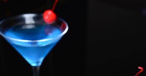 Due cocktail eleganti, uno blu e uno arancione, con ciliegie e fette d'arancia.