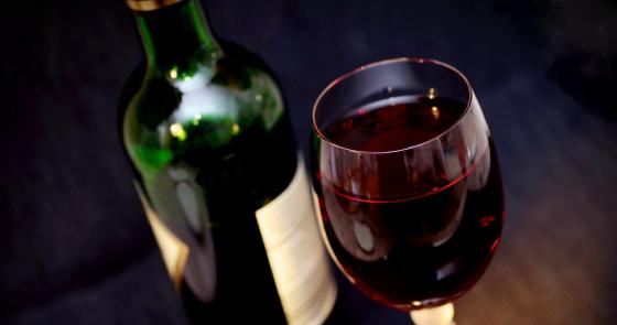 Calice di vino rosso accanto a una bottiglia, atmosfera elegante e raffinata.