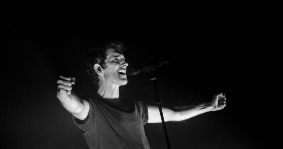 Cantante in bianco e nero, braccia aperte, esprime passione ed energia.