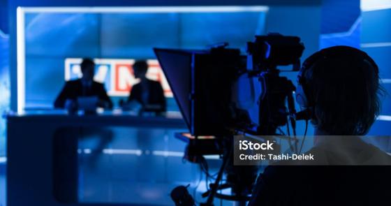 Studio televisivo, luci blu intense, atmosfera di concentrazione e professionalità.