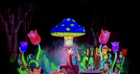 Scena magica con fiori giganti e personaggi fantastici in un'ambientazione incantata.
