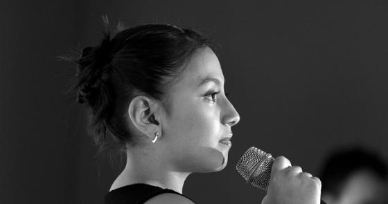 Giovane donna canta intensamente, microfono alla mano, emozione palpabile.