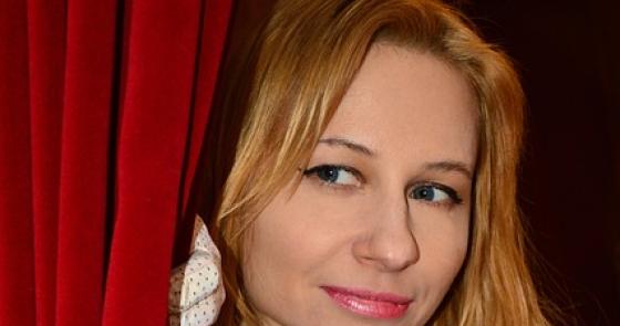 Donna elegante con guanti bianchi, sguardo misterioso dietro una tenda rossa.