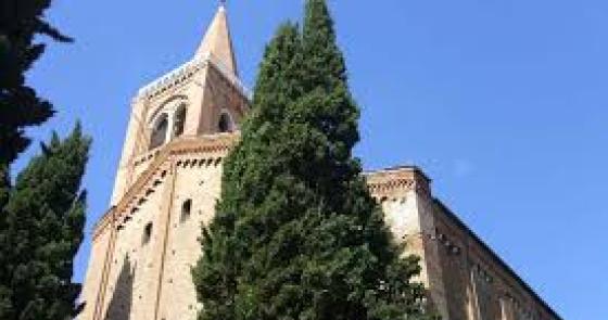 Campanile gotico svetta tra cipressi sotto un cielo azzurro.