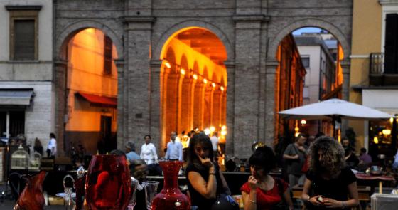 Mercato serale con vetreria colorata e luci calde sotto antichi archi.