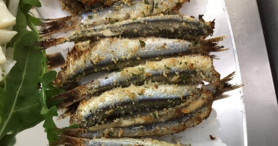 Alici al forno con panatura croccante, servite su un piatto bianco.